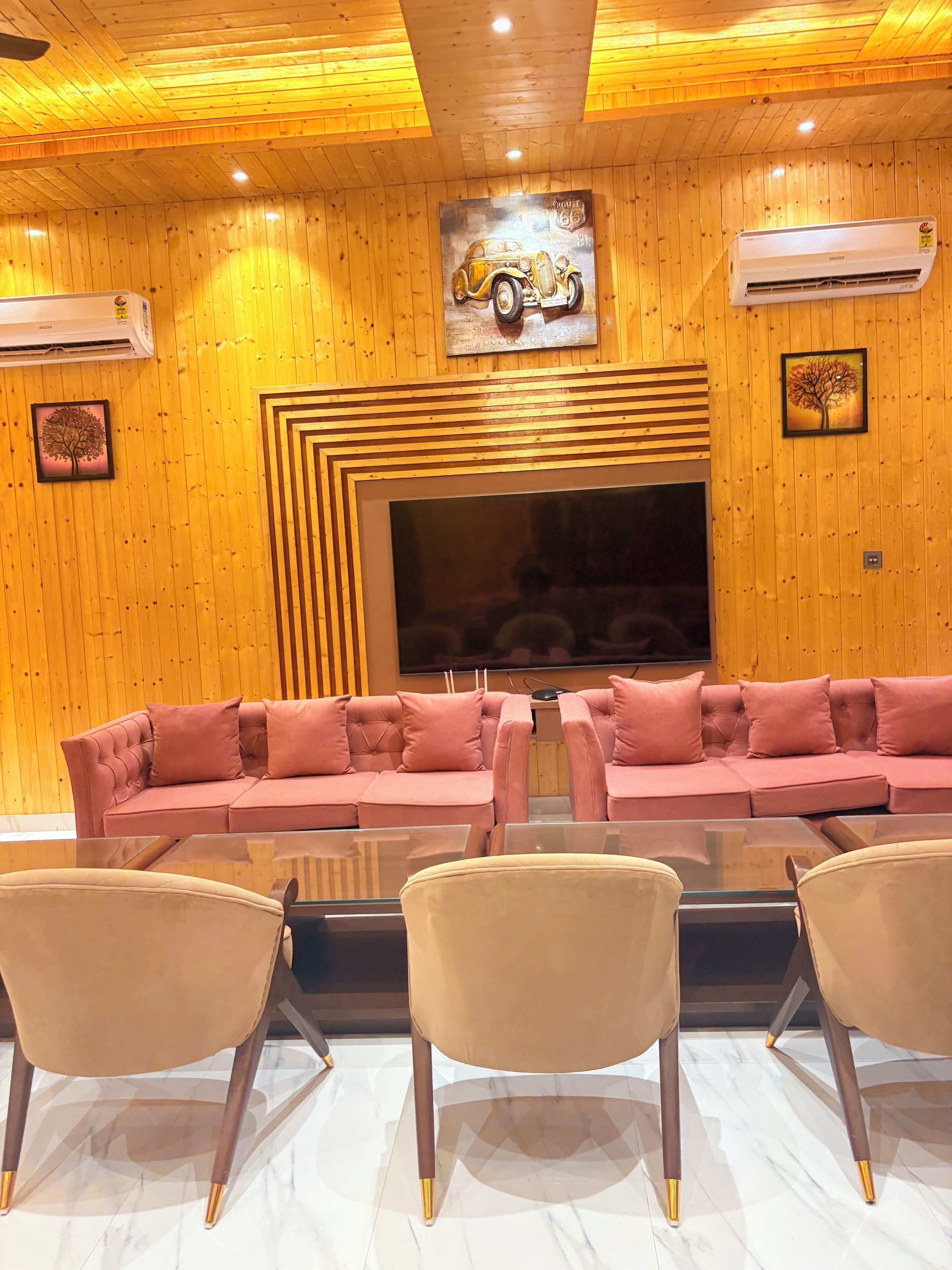 Un salon moderne doté d’un grand téléviseur à écran plat, d’un canapé d’angle rose et d’une table basse en verre.