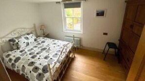 A bedroom with a bed, a window, a radiator, a wooden wardrobe, and a small chair.