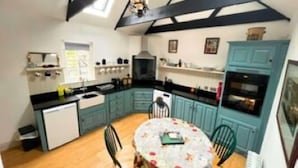 A kitchen with teal cabinets, a round table with floral tablecloth, and a ceiling fan.