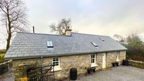 A stone building with a sloped roof, a gravel driveway, and a metal fence.