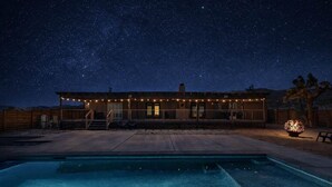 A house with a pool, string lights, and a starry night sky.