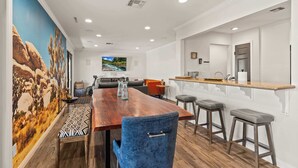 A modern kitchen with a wooden countertop, bar stools, and a large TV screen.