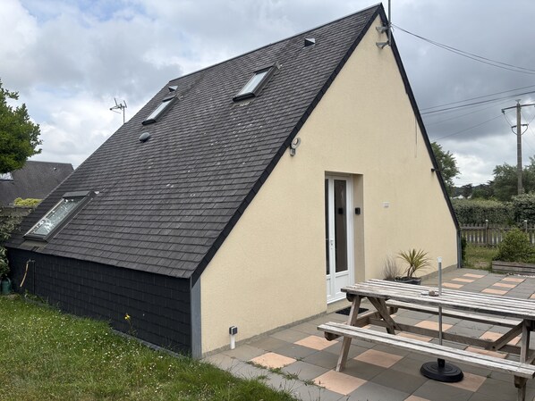 A house with a sloped roof, a small attached garage, and a patio area with a wooden table and benches.