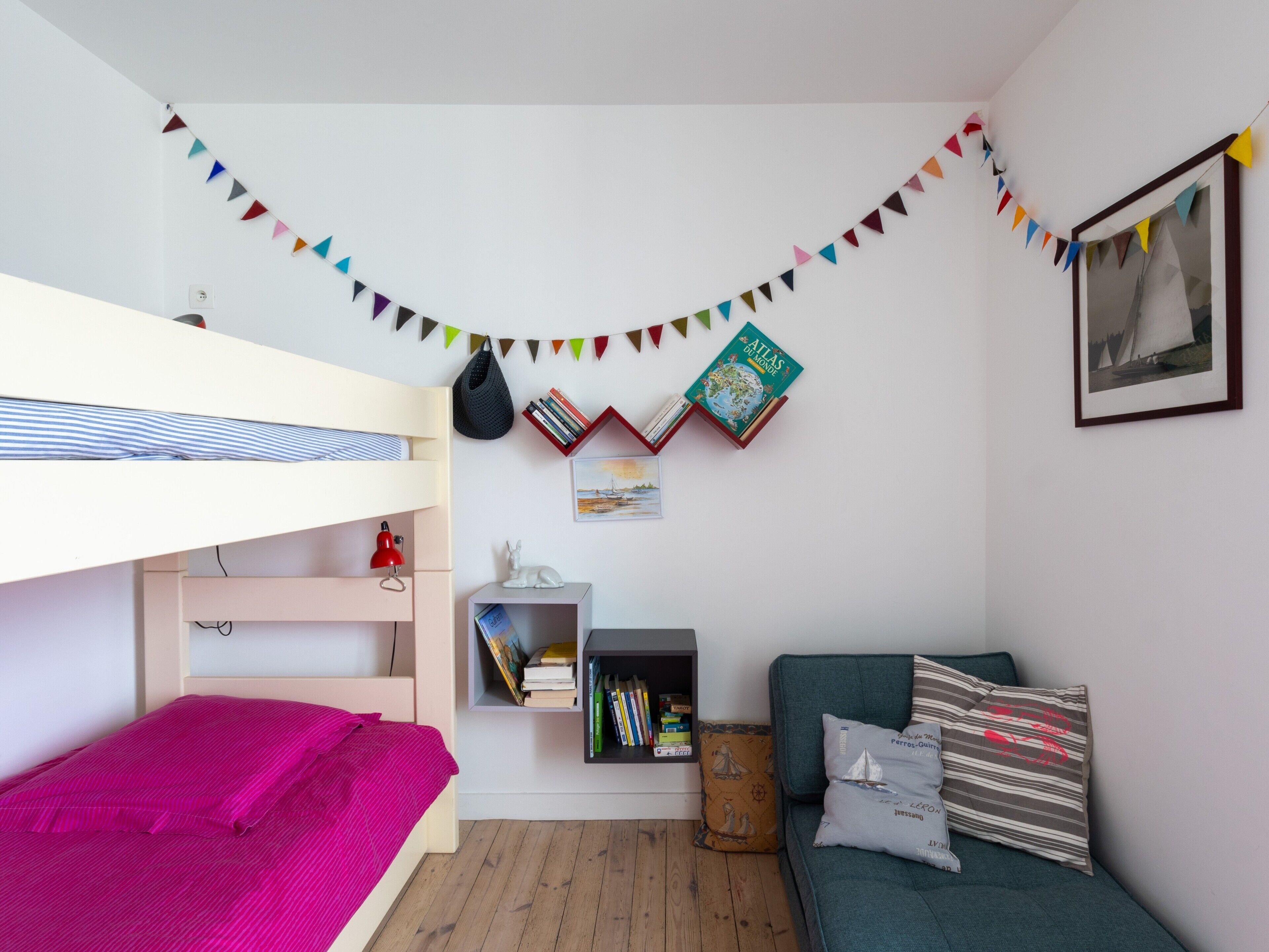 A room with a bunk bed, a desk with books, a green sofa, and a wall-mounted shelf.