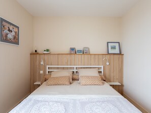 A bedroom with a wooden headboard, a bed with patterned pillows, a bedside lamp, and a shelf with framed pictures. - Charming Apartment in Locquirec with Sea View (Locquirec)