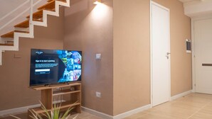 Un salon moderne avec un escalier, un téléviseur à écran plat, une table basse en bois et une plante en pot.