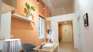Une chambre d’hôtel moderne avec un bureau en bois, une chaise grise, une lampe et une plante en pot.