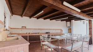 An outdoor kitchen with a tiled backsplash, wooden beams, and a metal table with benches. - Casa vacanza Margiulu’ (Partanna)