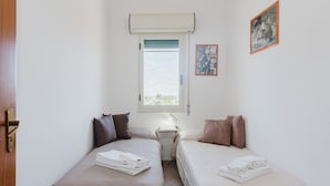 A small, clean room with two beds, a window, a door, and a wall-mounted air conditioner. - Casa vacanza Margiulu’ (Partanna)