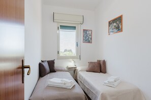 Una habitación con dos camas, una ventana con persianas, un cuadro en la pared y una puerta.