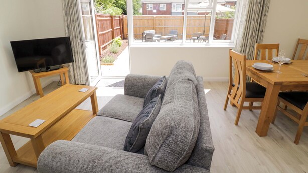 A living room with a grey sofa, wooden coffee table, and a TV on a stand. - 22 Old Chapel Close (Kidlington)