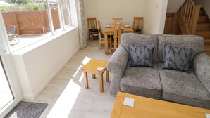 A cozy living room with a grey sofa, wooden coffee table, and a dining area with wooden chairs and a table. - 22 Old Chapel Close (Kidlington)