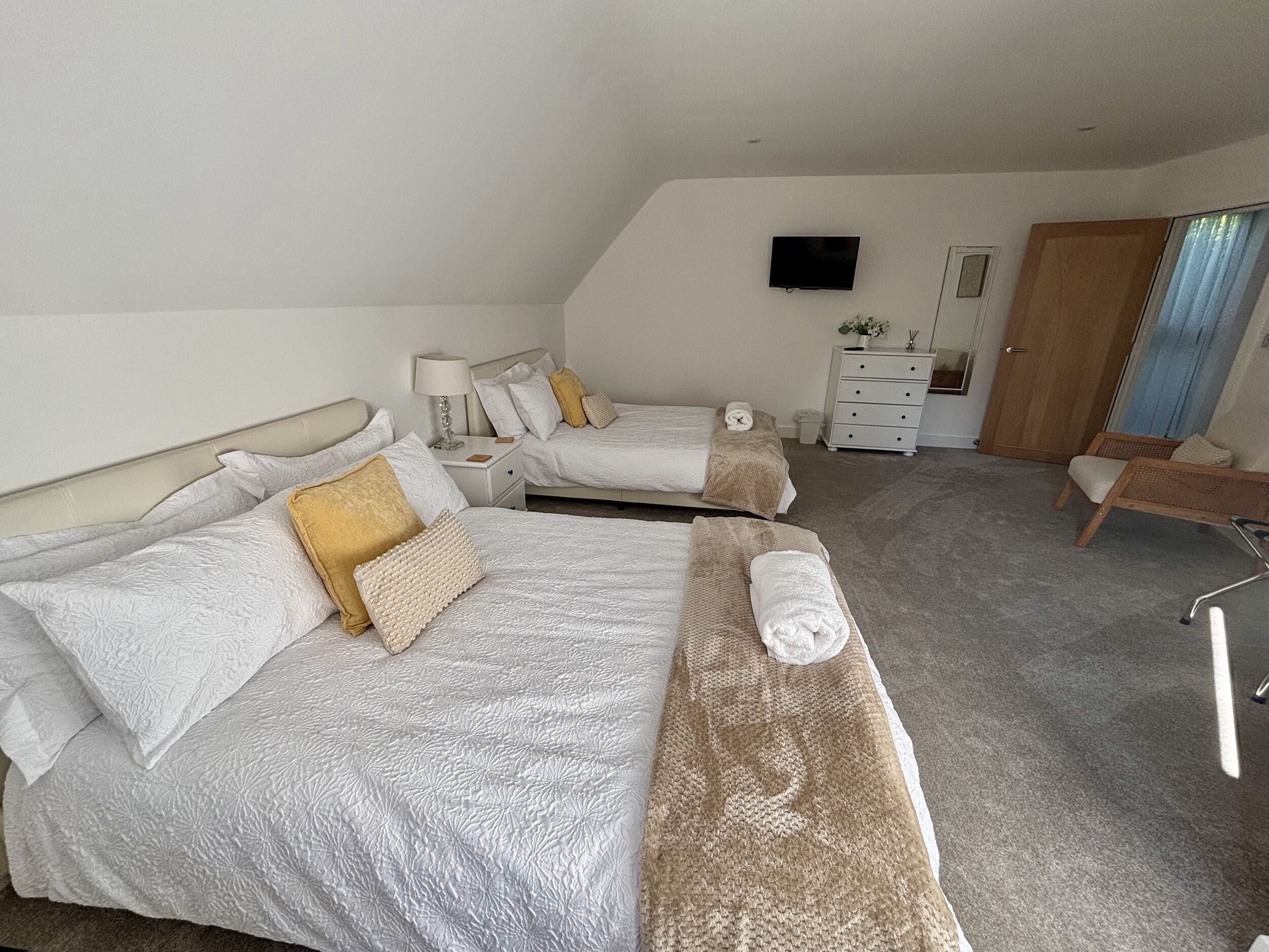 Quarto de hotel com duas camas, uma escrivaninha, uma cadeira, uma televisão e um guarda-roupa.