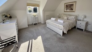A bedroom with a sloped ceiling, a bed with floral bedding, a nightstand, a dresser, and a window with curtains. - The Retreat (Ferndown)