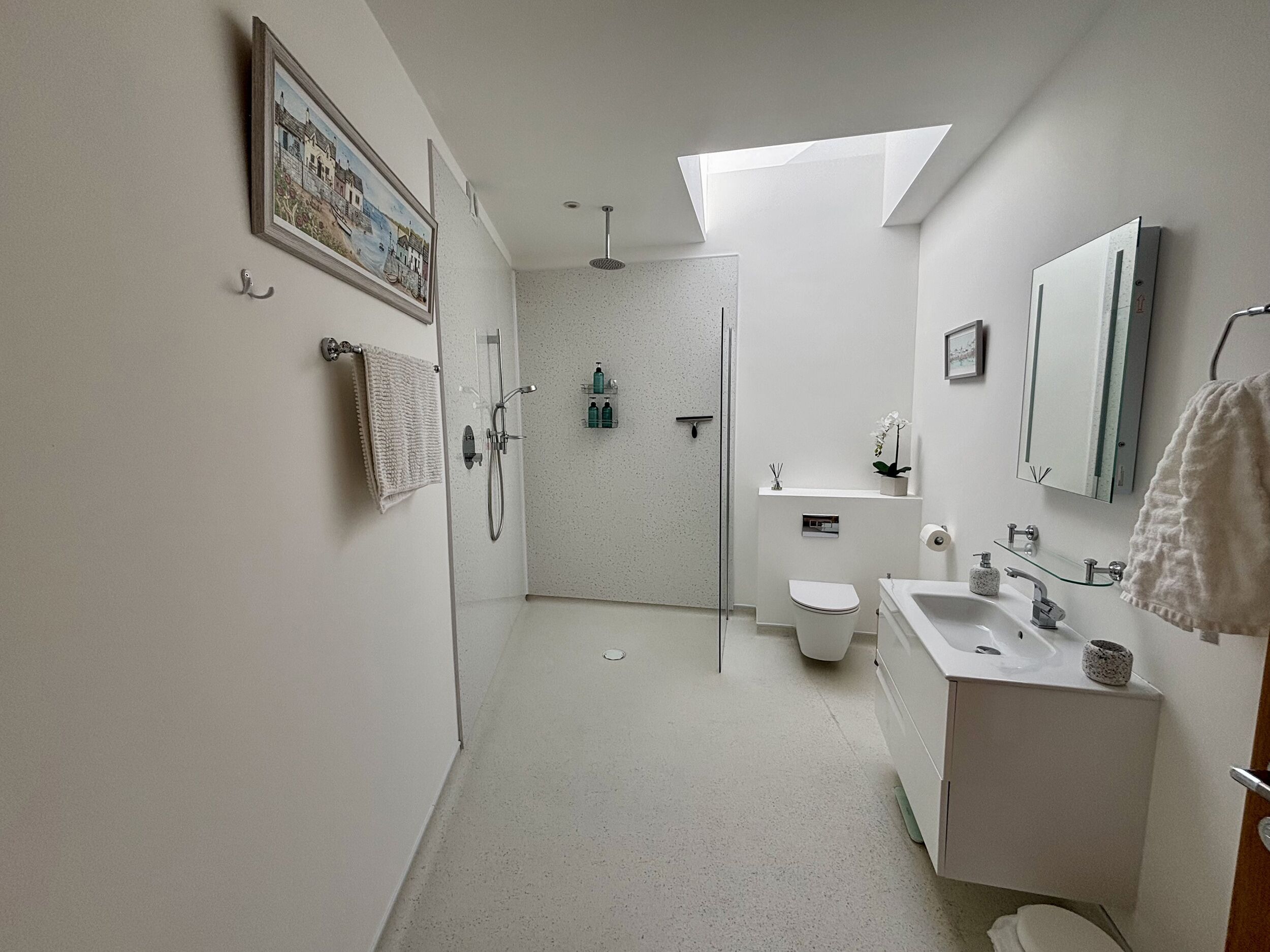 Ein modernes Badezimmer mit Dusche, Toilette, Waschbecken und einem Oberlicht.