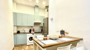 A modern kitchen with light blue cabinets, a wooden dining table with white chairs, and a small chalkboard with a welcome message. - Very central studio with A/C, equipped kitchen, and elevator. (Málaga)