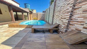 A backyard with a swimming pool, wooden loungers, and a tiled patio. - Casa em Natal com Piscina a 290m da Praia (Natal)