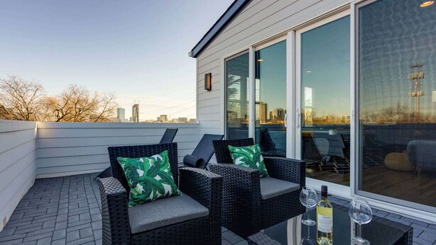 A rooftop patio with wicker furniture, a glass table, and a bottle of wine. - 4BR Retreat for 12 w Balcony, Mins to Broadway! (Nashville)
