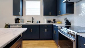 A modern kitchen with dark cabinets, a stainless steel range, and a window with blinds. - 4BR Retreat for 12 w Balcony, Mins to Broadway! (Nashville)
