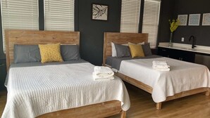 Two wooden beds with grey and yellow bedding, a small artwork on the wall, and a bathroom with a sink and mirror. - 4BR Retreat for 12 w Balcony, Mins to Broadway! (Nashville)