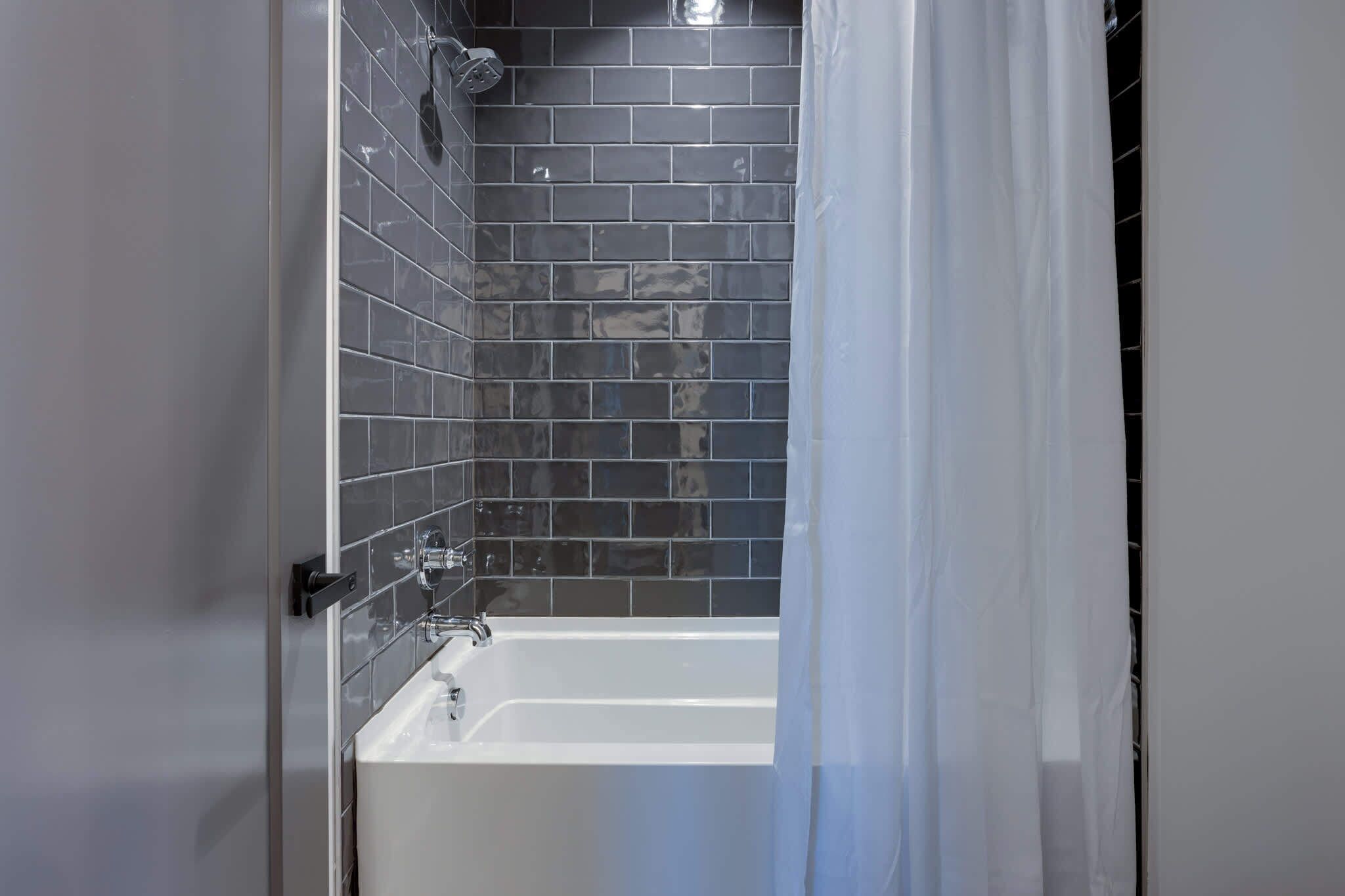 A bathroom with a white bathtub, dark tiled walls, and a shower area.