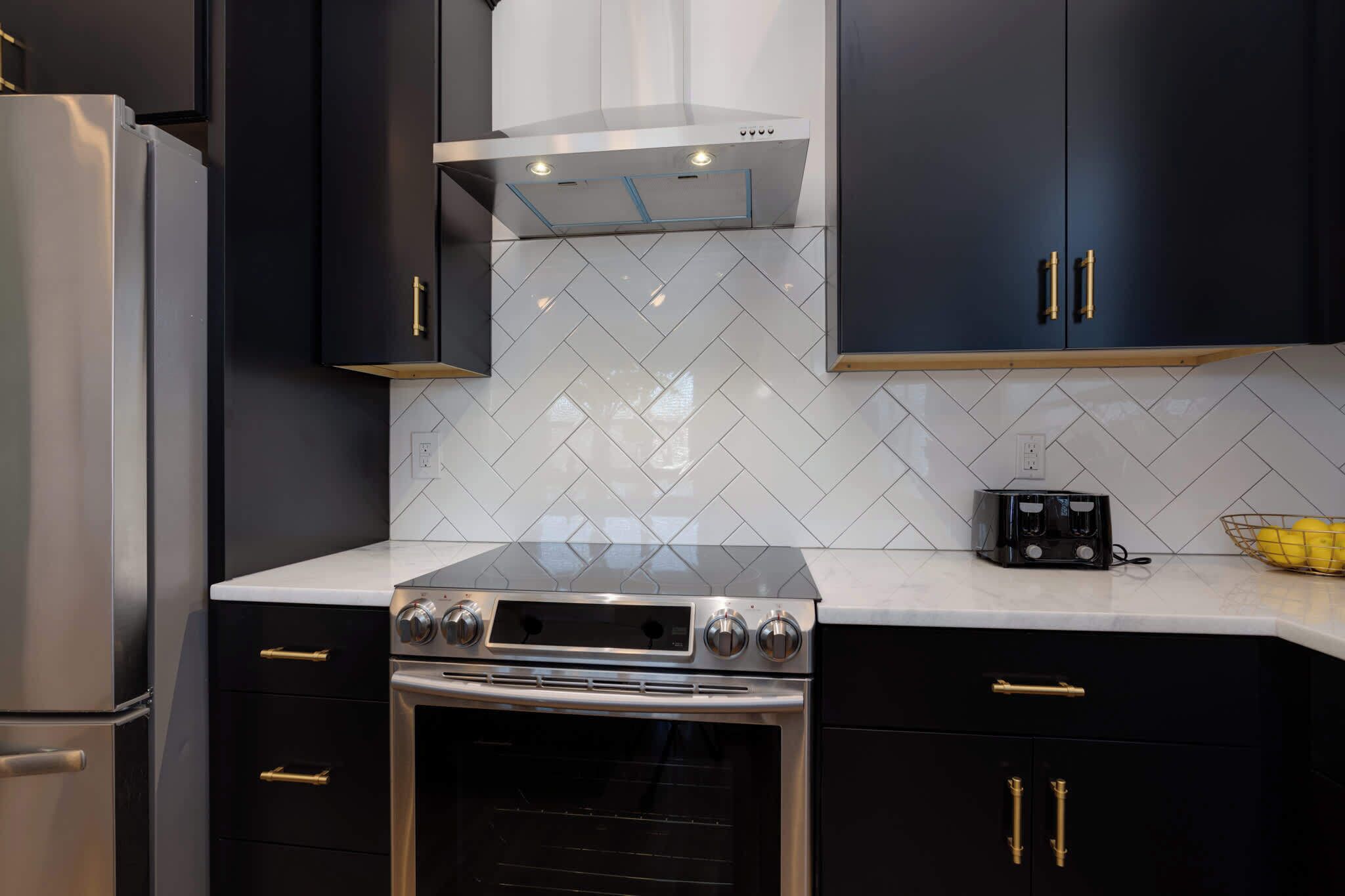 A modern kitchen with black cabinets, a stainless steel refrigerator, a built-in oven, and a toaster on the countertop.