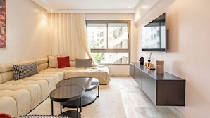 Una sala de estar moderna con un sofá, dos mesas auxiliares, un ventanal con cortinas y un televisor montado.
