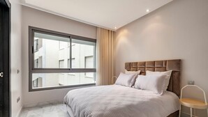 Un dormitorio con un ventanal grande, una cama con cabecero y una silla.