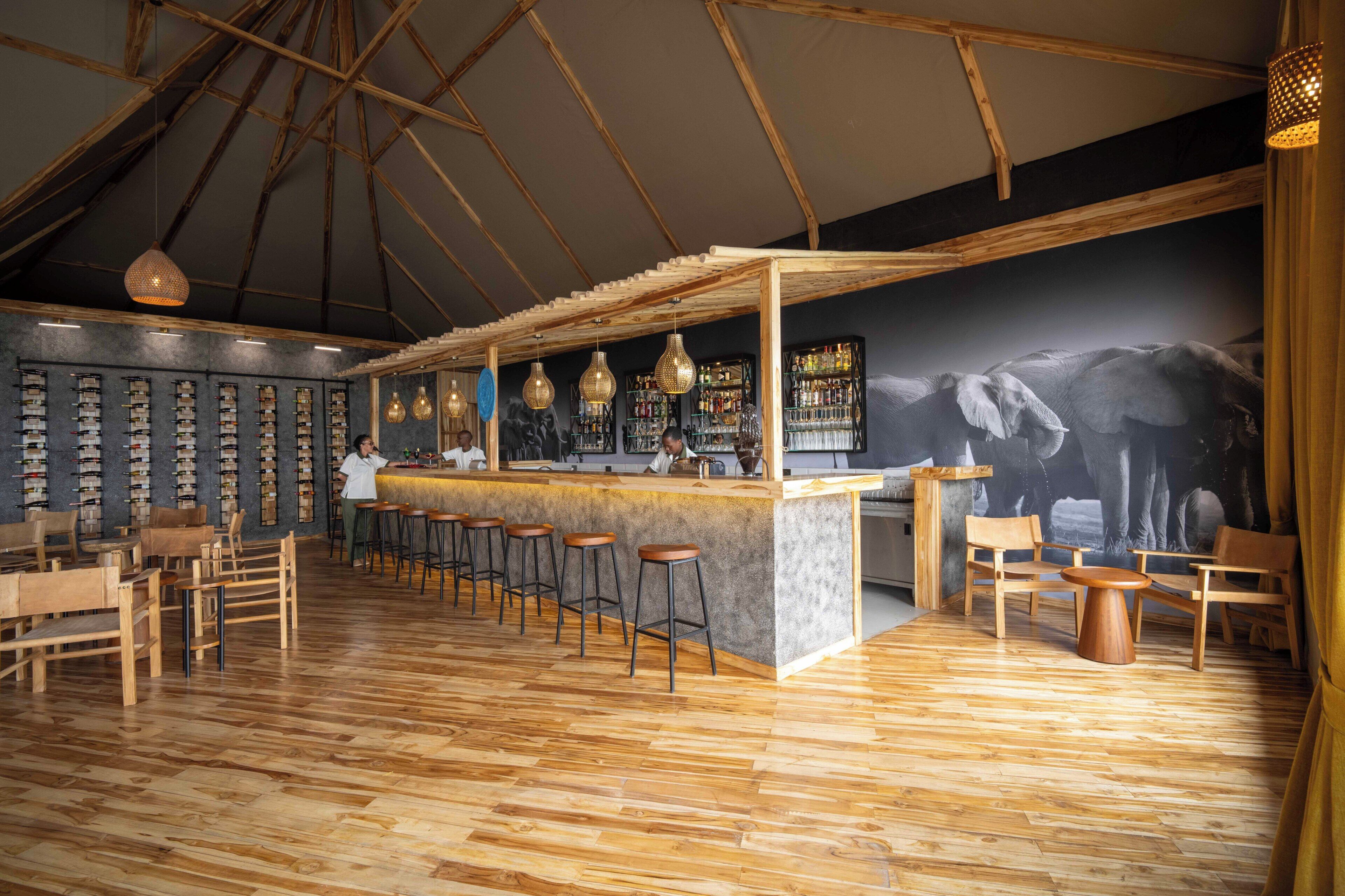 A bar area with wooden flooring, bar stools, and a counter.