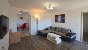 A modern living room with a sofa, a coffee table, and a dining area with red chairs. - Apartment Mare e Vista (Rovinj)