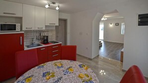 A compact kitchen with white cabinets, a red countertop, and a patterned tablecloth. - Apartment Mare e Vista (Rovinj)