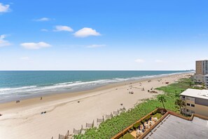 A beach with a view of the ocean, a sandy beach, and a building with a parking area.