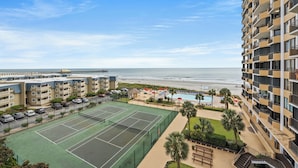 Um hotel com vários andares, quadra de tênis, piscina e vista para a praia.