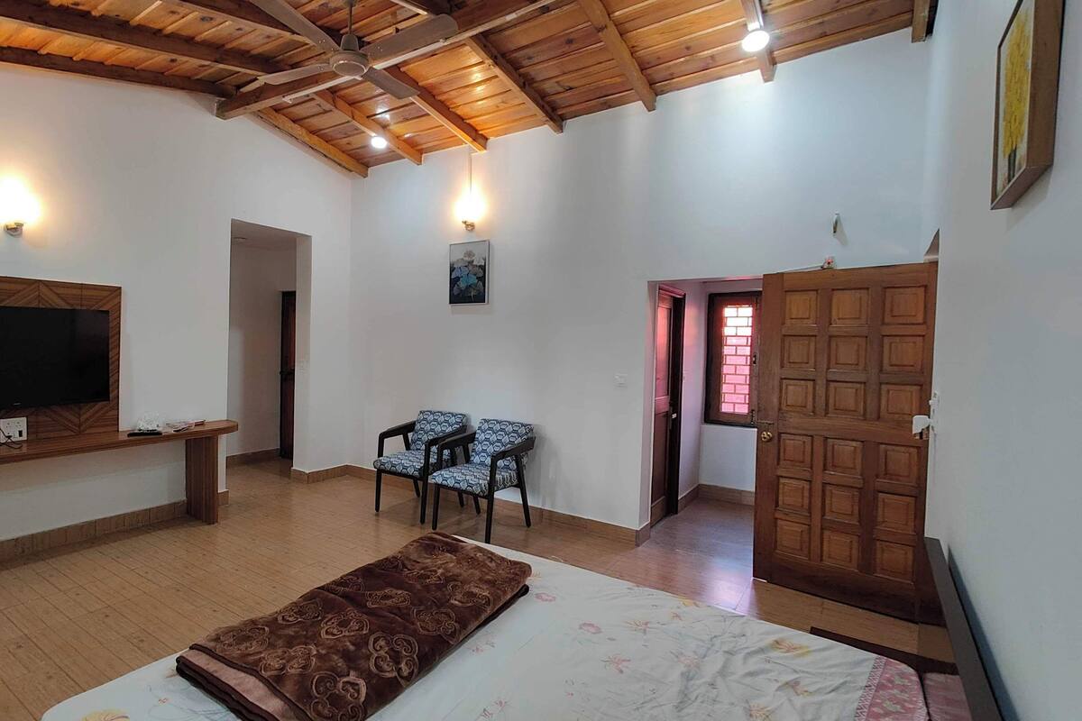 A room with a wooden ceiling, a flat-screen TV mounted on a wooden wall, a sofa, a patterned rug, and a door with a window.