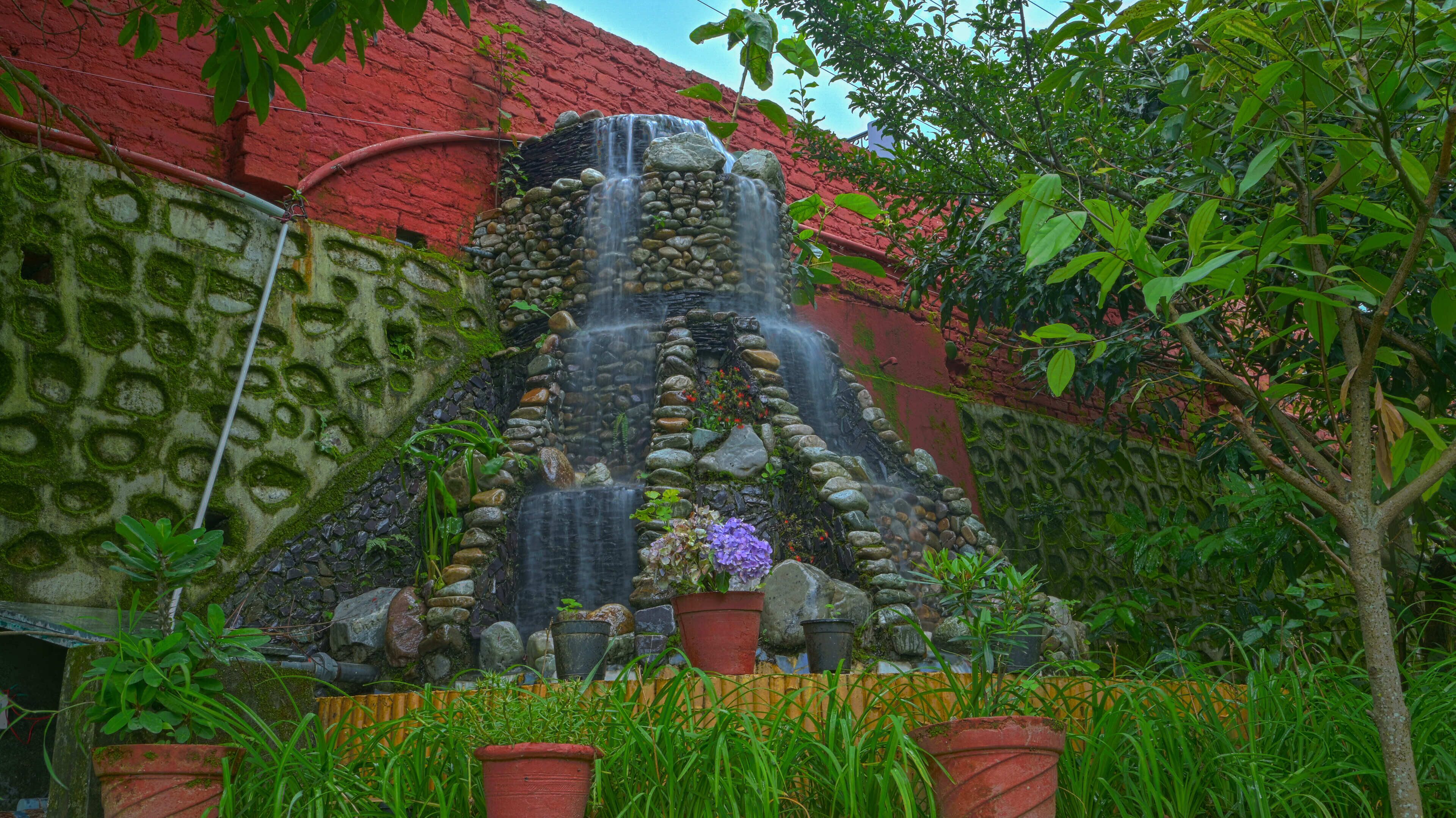 A waterfall feature with a stone structure, surrounded by potted plants and greenery.