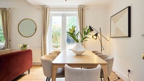 Ein Essbereich mit einem Holztisch, sechs Stühlen, einem roten Sofa, einem runden Spiegel, einer Pflanzvase und einem gerahmten Bild an der Wand.
