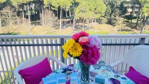 A balcony with a table set for two, featuring a vase of flowers, a small figurine, and a brochure. - Luminous Flat With Balcony-beahost (San Michele al Tagliamento)