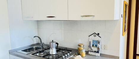 A modern kitchen with white cabinets, a gas stove, a sink, and a decorative house-shaped shelf.