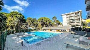 A swimming pool with a tiled deck, surrounded by trees and a multi-story building. - Luminous Flat With Balcony-beahost (San Michele al Tagliamento)