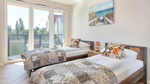 Een slaapkamer met twee bedden, een groot raam en een schilderij van een kustgezicht.