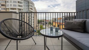 A balcony with a black wicker chair, a round glass table, and a grey sofa.