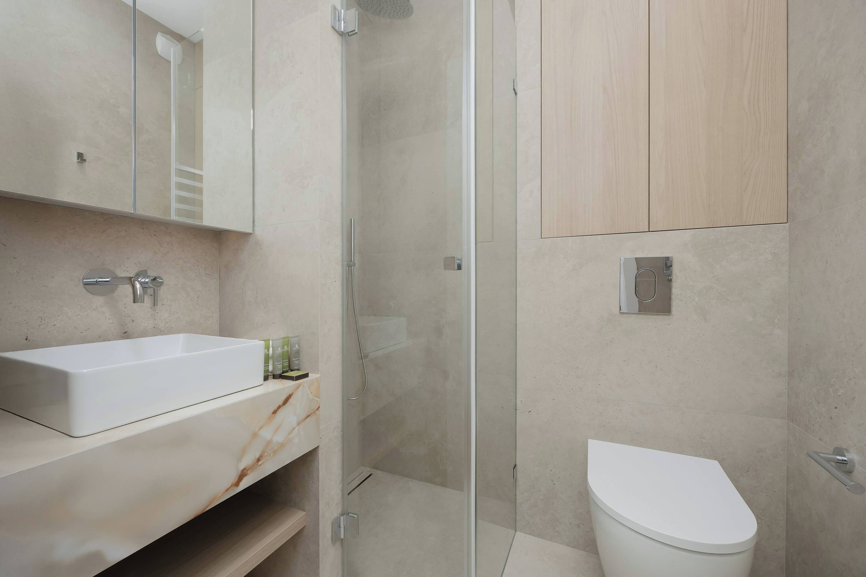 Un baño moderno con ducha de vidrio, lavamanos blanco y retrete.