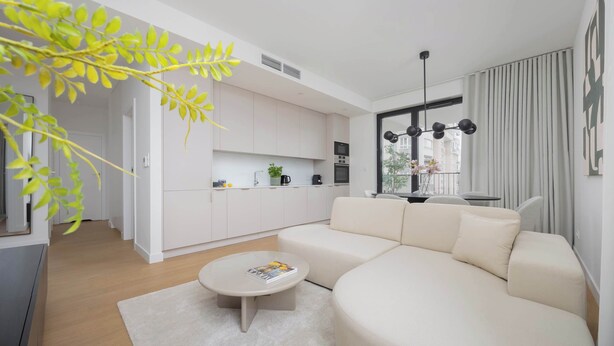 A modern living room with a beige sofa, a round coffee table, and a kitchen in the background.