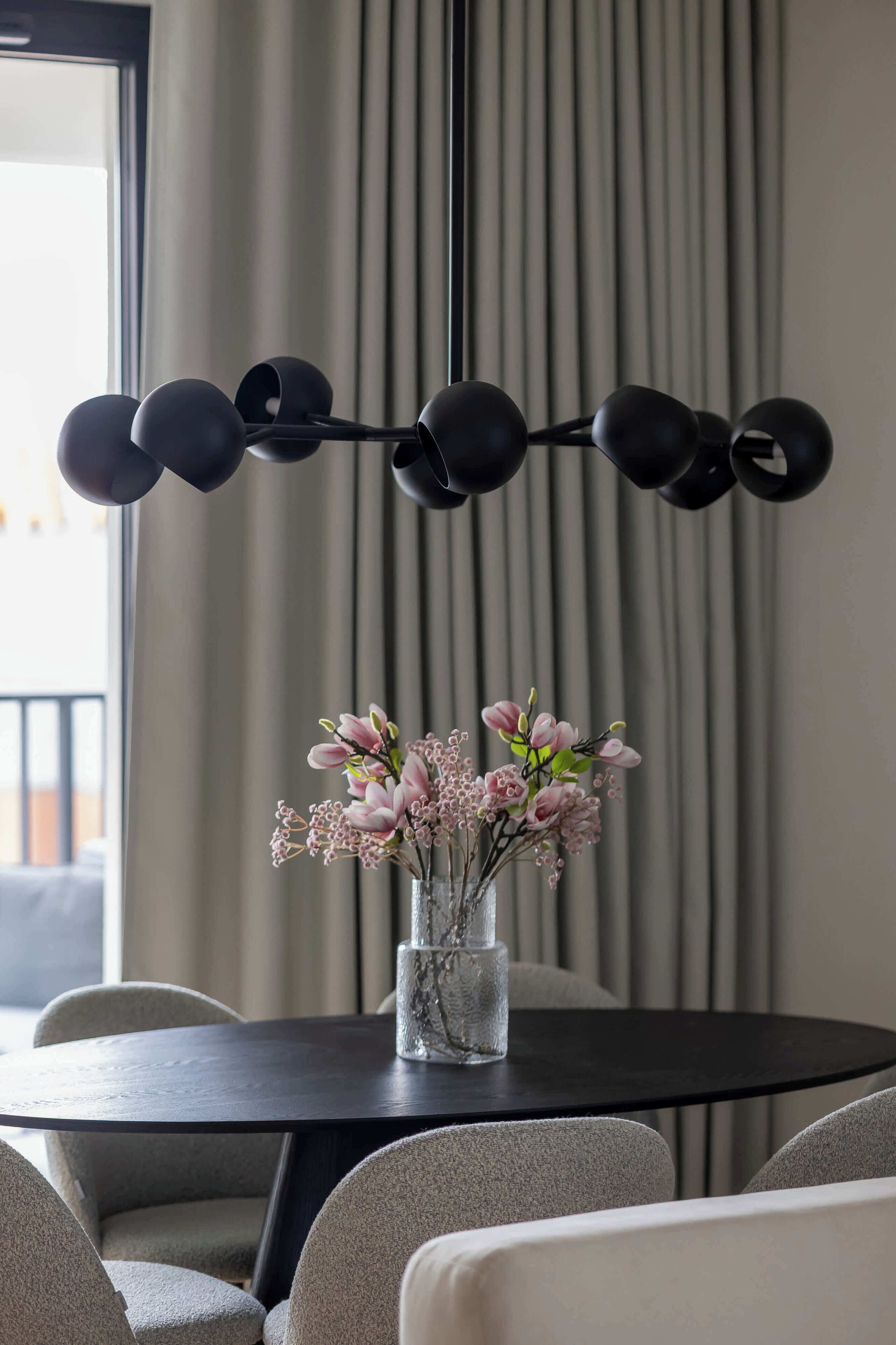 Un coin repas avec une table ronde, des chaises, un vase de fleurs et un luminaire suspendu moderne.