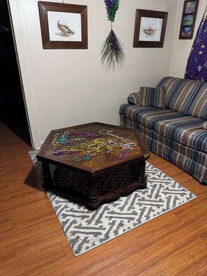 Una mesa de centro de madera con cuentas de colores, un tapete estampado, un sofá a rayas y obras de arte enmarcadas en la pared.