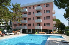 A multi-story building with balconies, a swimming pool, and lounge chairs. - Bright Apartment With Balcony-beahost (San Michele al Tagliamento)