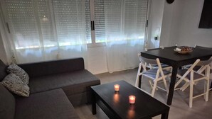 Ein modernes Wohnzimmer mit einer Couch, einem kleinen Tisch mit Kerzen und einem Essbereich mit Stühlen.