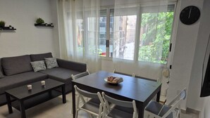 Ein modernes Wohnzimmer mit einer Couch, einem Couchtisch, einem Esstisch mit Stühlen, einem Fenster mit Vorhängen und einer Wanduhr.