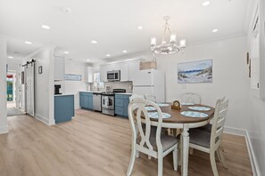 Une cuisine moderne avec des meubles blancs, un four à micro-ondes et un réfrigérateur. On y trouve une table à manger avec des chaises et un lustre au-dessus.