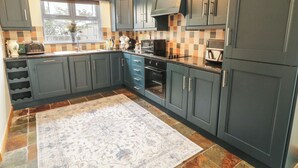A kitchen with dark cabinets, a tiled backsplash, a built-in oven, and a window with blinds. - The Sperrin Getaway (Omagh)